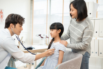 Asian female doctor smiling while examining a young girl, .Healthcare worker checking the health of a patient girl..