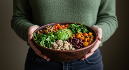 Woman holds bowl of colorful salad with avocado grains and vegetables.