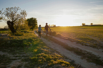 Couple walking with bicycles on country road at sunset