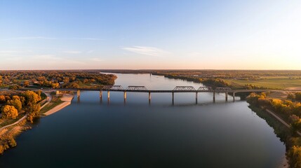 Fototapeta premium A panoramic aerial capture of a bridge spanning a calm river, the geometric lines of its structure contrasting beautifully with the natural curves of the water. 