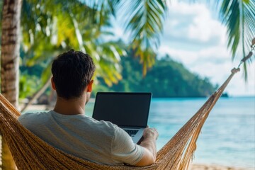 Man using laptop in hammock on beach with ocean view for travel blogs and vacation rentals