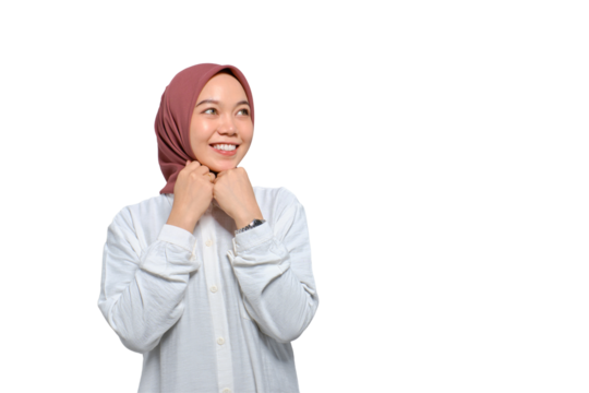 Smiling young Asian Muslim woman pressing hands together under chin and looking away at copy space isolated on transparent background