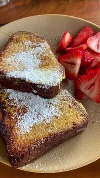 Delicious french toast and strawberries plate is served on table filmed from phone pov of food vlogger or critic. Social media content style or user generated. Tasty food in cafe or breakfast bistro