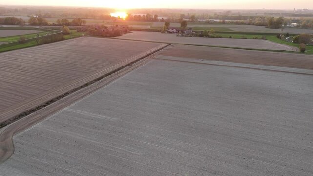 Early evening light illuminates freshly harrowed farmland near the Po River between Olza and Cremona, with orthogonal field lines and subtle elevation changes, aerial view, real time