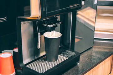 Coffee machine filling black cup on counter, close-up view.