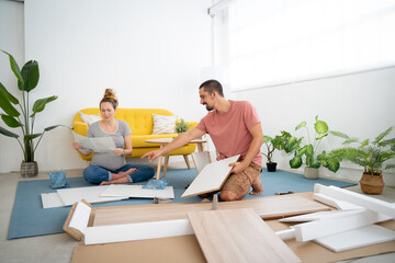 Couple with pregnant woman is joyfully assembling furniture together in their living room. High quality photo