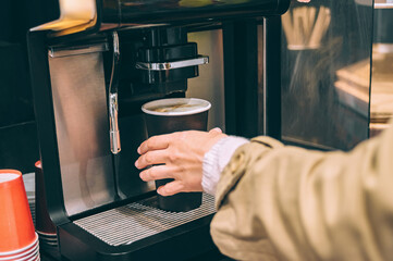Close-up of hands using coffee machine for paper cup.