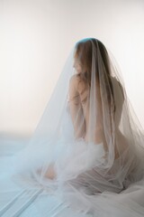 Sensual beauty draped in delicate fabric poses in a serene setting