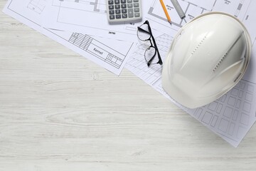 Different architectural drawings, hard hat, pencil, vernier caliper, calculator and glasses on light wooden table, flat lay. Space for text
