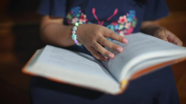 A child's small hands with aesthetic accessories flipping through book pages, conveying that learning knows no boundaries of time, place, or person. Inspiring educational concept