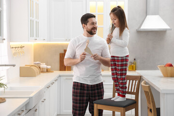 Happy father and his daughter wearing stylish pajamas having fun with cookware in kitchen