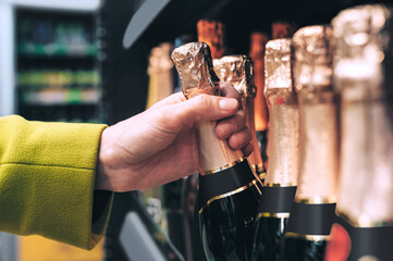 Hand taking sparkling wine bottle with gold foil from shelf.
