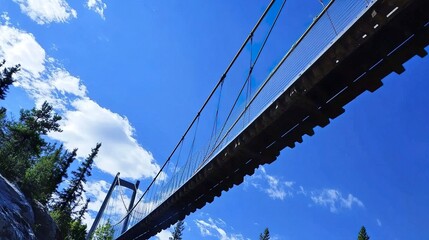 Naklejka premium Suspension bridge viewed from below with its cables stretching towards a crisp blue sky, showcasing geometric precision and structural beauty. 