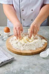 Kneading shortcrust pastry by hand on a wooden board on a grey concrete background. Different types of dough and their preparation techniques.