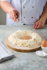 Kneading shortcrust pastry by hand on a wooden board on a grey concrete background. Different types of dough and their preparation techniques.