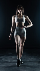 Young beautiful woman with athletic body on dark background. Fitness girl