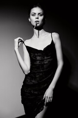 Stylish young woman in a sleek black dress posing confidently with a cigarette, showcasing elegance and modern fashion. Dramatic lighting creates an intense atmosphere.