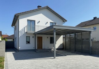 View of a two story house with a carport and a small balcony on a sunny day with a clear blue sky
