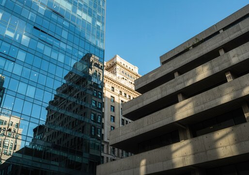 Low angle view of modern glass building reflecting older architecture under a clear blue sky today