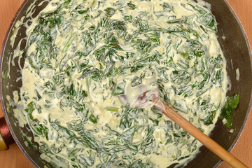 A top-down view shows creamy spinach being stirred in a dark pan with a wooden spoon