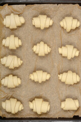 An overhead close-up of raw, rolled croissant dough pieces arranged on parchment paper before baking