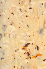A detailed close-up shows the surface texture of white cake batter with scattered walnuts, dark chocolate pieces, and bright orange zest