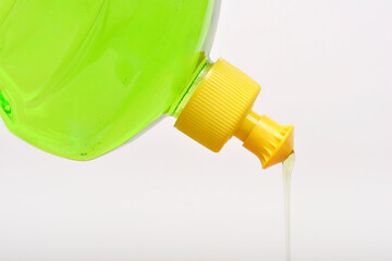 Tilted clear plastic bottle with a yellow cap pours a stream of light green dish soap