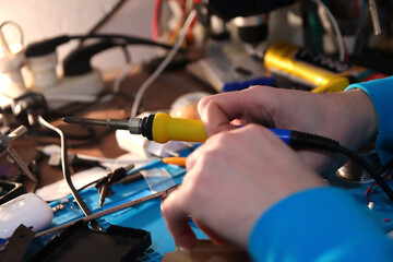 Close-up of a hand soldering a phone circuit board with a yellow soldering iron and copper bit....
