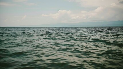 Calm expanse of open ocean under a cloudy sky, distant mountains visible