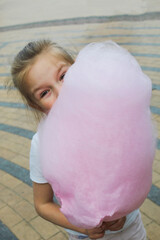 Little girl enjoying pink cotton candy outdoors..