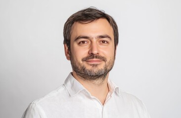 Obraz premium Formal portrait of a man. Light-skinned man with short brown hair and a trimmed beard, wearing a white button-up shirt, front-facing in a neutral pose against a light gray background