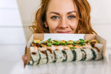 Close-up. A cheerful woman holds a set of delicious sushi with a happy face. On a light background.