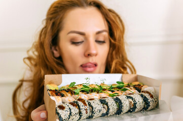 Close-up. A cheerful woman holds a set of delicious sushi with a happy face. On a light background.