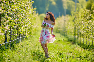 Full body portrait of a beautiful woman in a dress in a blooming apple orchard on a sunny spring day