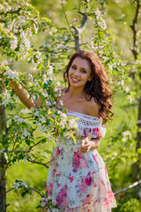 portrait of a beautiful woman in a dress in a blooming apple orchard enjoying a sunny spring day
