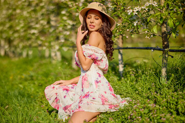 portrait of a beautiful woman in a dress in a blooming apple orchard enjoying a sunny spring day