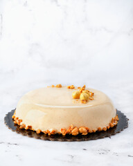 Refined French-style praline cake with hazelnuts on white marble background. Glazed finish, front view, clean layout with copy space. Ideal for packaging, branding, or pastry menus.