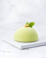 Elegant individual green mousse cake with velvet texture, mint leaves and golden pearls. Side view on white marble slab with copy space. Ideal for premium packaging and editorial content.