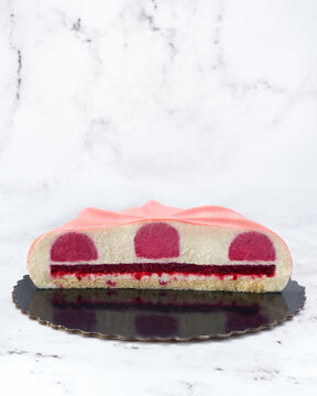 Artistic raspberry and white chocolate mousse cake with velvet texture and geometric cut. Cross-section showing layered filling on marble background. Ideal for editorial or branding use.