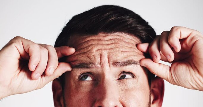 Skincare, man and check for wrinkles, studio or worried for fine lines, hands or routine in morning. White background, person and inspection of forehead, scared or thinking of treatment for antiaging
