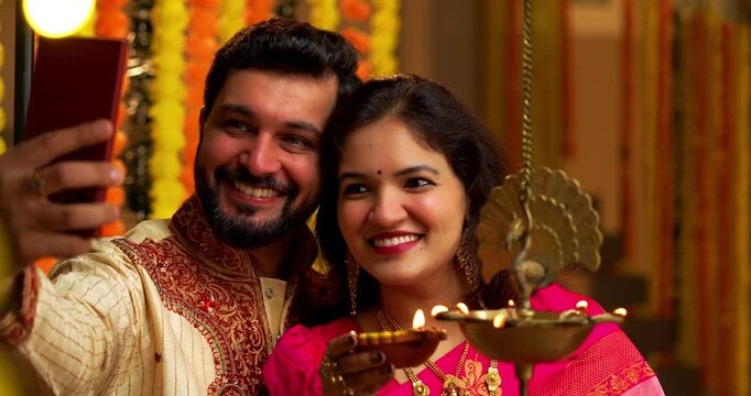 Taking Selfie Lighting Diwali Samai, Indian Married Couple in Saree and Kurta Celebrates Festival Night by Lighting Traditional Brass Oil Lamp as Husband Clicks Selfie on Smartphone with Smiles