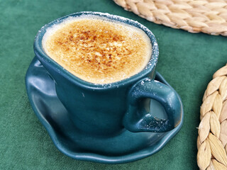 Green teacup filled with coffee creme brulee, its caramelized top inviting a taste. Green velvet surface adds a touch of luxury