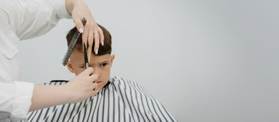 A photo from the life of a hairdresser's client, a dark-haired boy. A female hairdresser at work, a comb, scissors. Short haircut in a modern style for children.