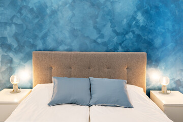 Close up of  bed in minimal, modern and luxury bedroom, Grunge Blue wall. Bedside tables Modern lamps.