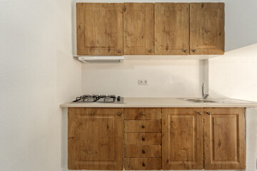 Modern small kitchen with wooden cabinets, gas stove, and stainless steel sink. Compact and minimalistic kitchen design in natural tones.