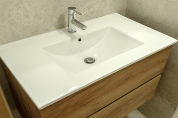 Modern white ceramic bathroom sink with wooden vanity cabinet and chrome faucet. Contemporary and clean design in a tiled bathroom setting.