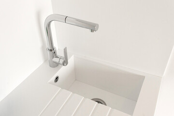 Contemporary minimalist kitchen sink in a clean white setting, featuring a sleek chrome faucet with a modern geometric design. 