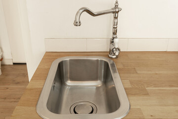 Modern stainless steel kitchen sink with a vintage-style chrome faucet, set in a wooden countertop. Minimalist interior design with clean lines and natural materials, creating a bright and functional