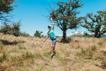 A female slackliner performs acrobatic poses and splits on a slackline stretched between trees on a...