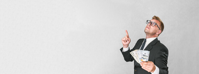Banner, Businessman in a suit shows thumbs up and holds american dollars in his hands on a...